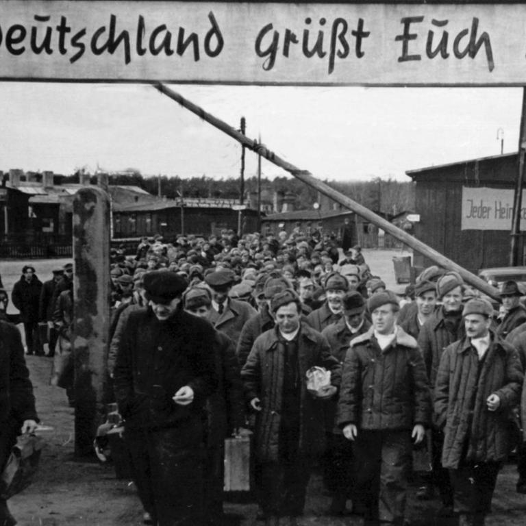 "Deutschland grüßt Euch" steht auf einem Schild über dem geöffneten Schlagbaum des Entlassungslagers Gronenfelde bei Frankfurt an der Oder. Die aus russischer Kriegsgefangenschaft entlassenen Heimkehrer treten von hier aus die Reise in ihre Heimatorte an. Aufgenommen am 12. April 1949.