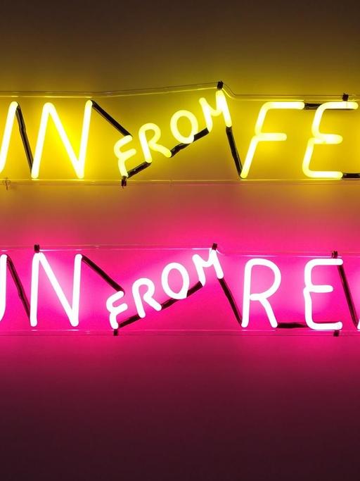 Zu sehen ist eine neonfarbene Leuchtinstallation in der Londoner Galerie Tate Modern. Zu lese ist: "Run From Fear, Fun From Rear".