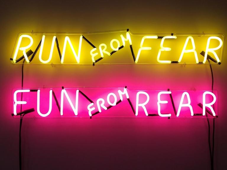 Zu sehen ist eine neonfarbene Leuchtinstallation in der Londoner Galerie Tate Modern. Zu lese ist: "Run From Fear, Fun From Rear".
