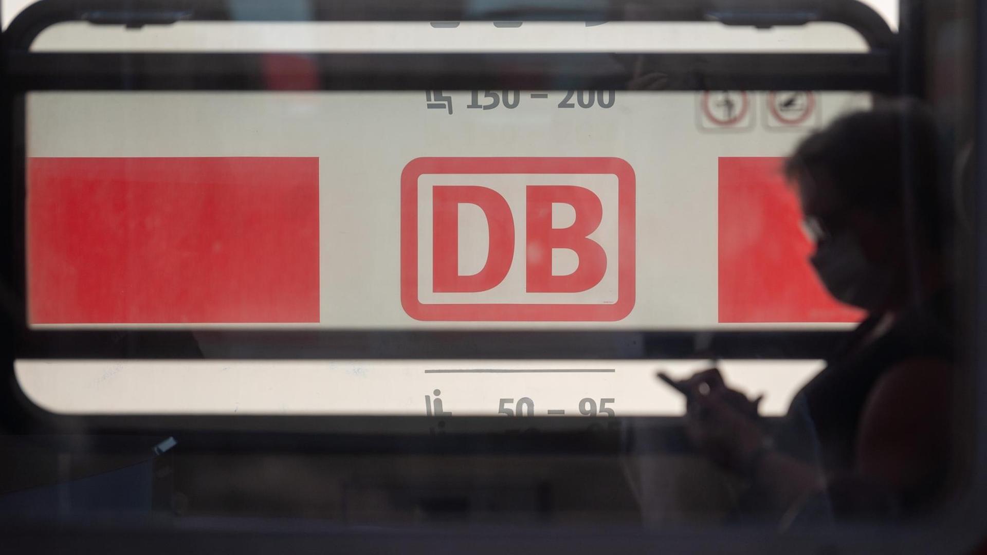 Ein Reisender mit Mund- und Nasenschutz sitzt in einem Zug der Deutschen Bahn, hinter dem ein ICE steht. Ein Reisender mit Mund- und Nasenschutz sitzt in einem Zug der Deutschen Bahn, hinter dem ein ICE steht.