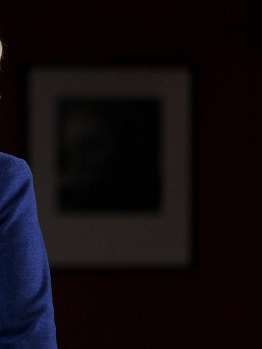 Eine Rückansicht Angela Merkels vor schwarzem Hintergrund.