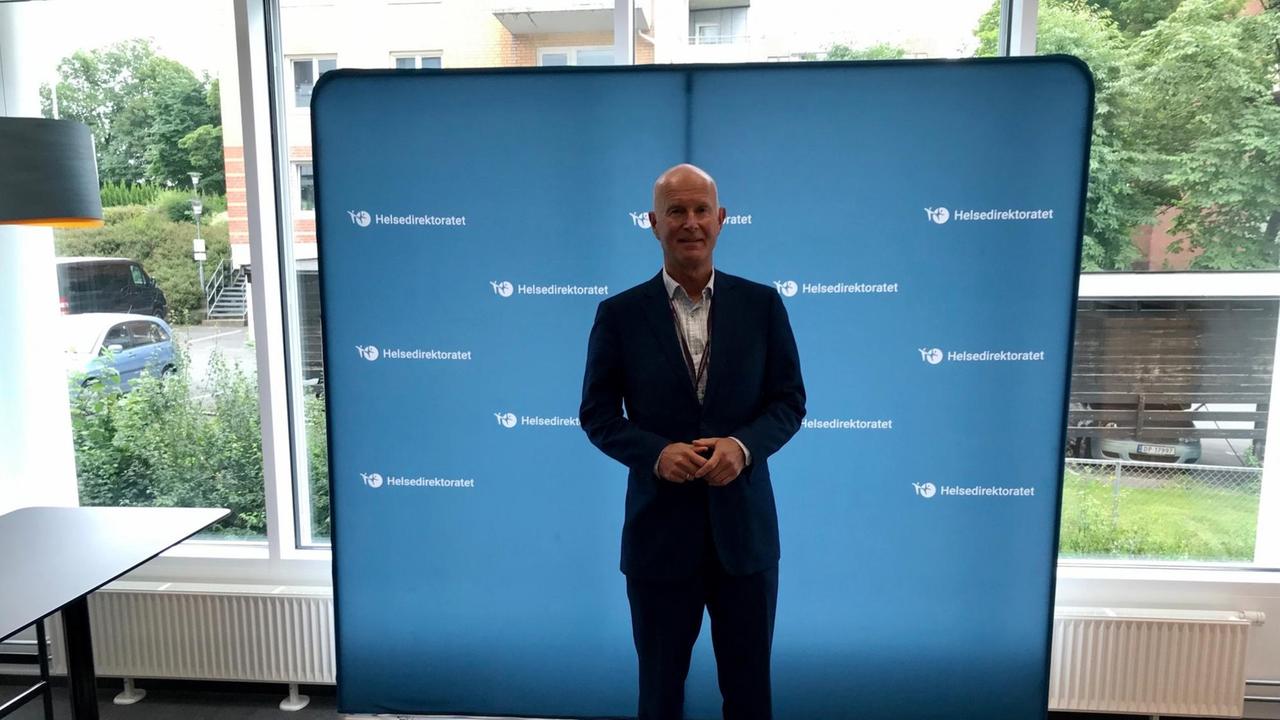 Ein kahlköpfiger Mann in Anzug steht vor einer großen blauen Leinwand. Ein kahlköpfiger Mann in Anzug steht vor einer großen blauen Leinwand.