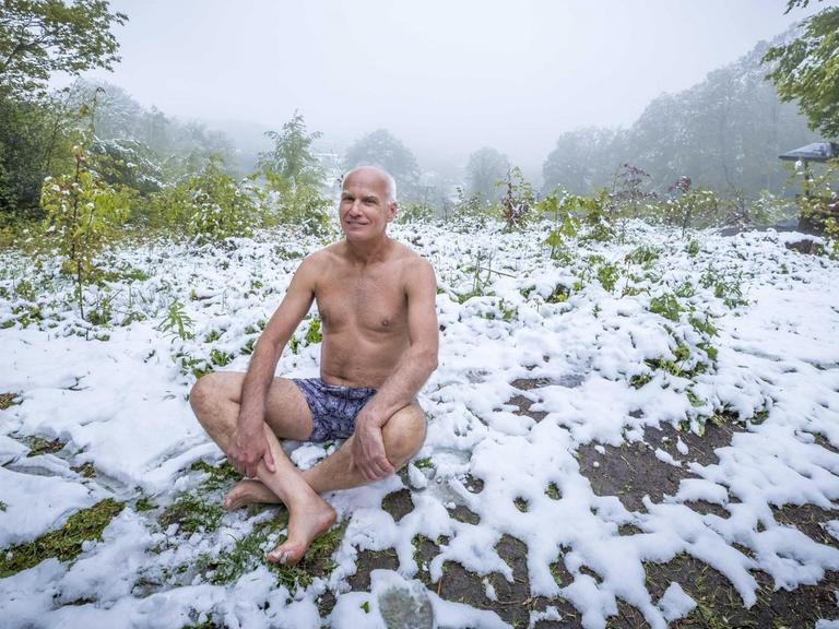 Ein Mann sitzt in Unterhose im frisch gefallenen Schnee.