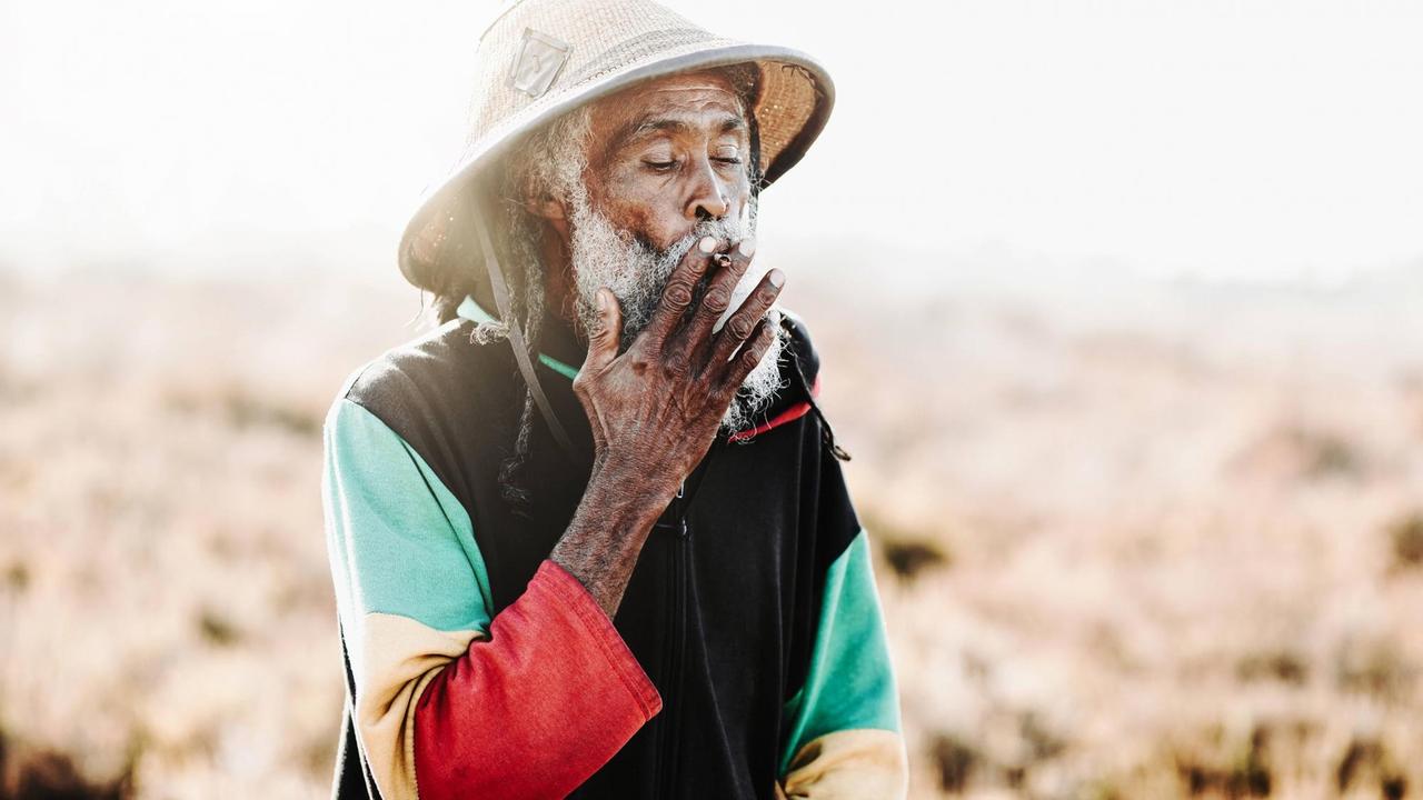 Ein fröhlicher alter Rastafari mit Dreadlocks raucht Cannabis.