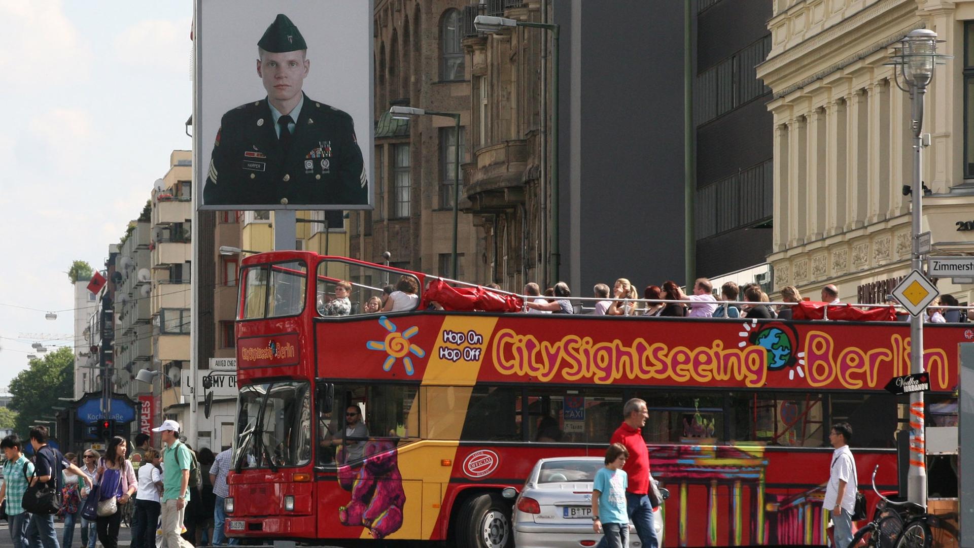 Ein knallroter Bus mit Touristen fährt über die Friedrichstraße am ehemaligen Checkpoint Charlie in Berlin-Mitte. Ein knallroter Bus mit Touristen fährt über die Friedrichstraße am ehemaligen Checkpoint Charlie in Berlin-Mitte.