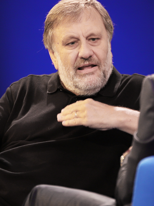 Slavoj Žižek gestikuliert auf einem Sofa