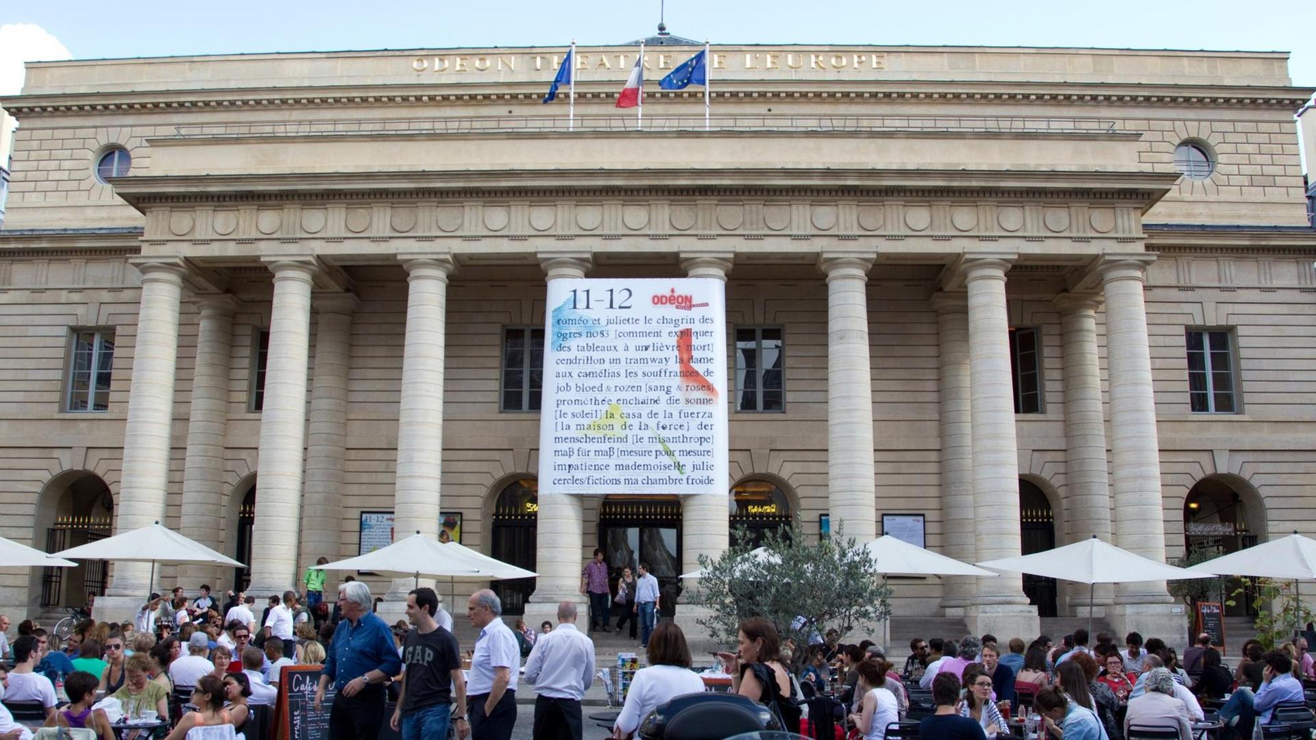 Blick auf das Théâtre de l'Odéon in Paris, Frankreich. Davor sitzen Menschen auf einem Platz an Tischen.