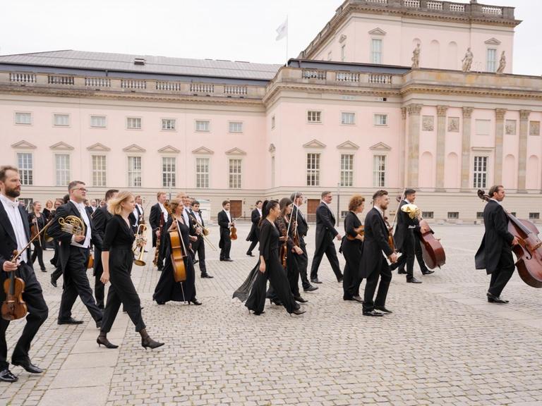 Musiker der Staatskapelle Berlin laufen vor dem Opernhaus mit ihren Instrumenten auf den Bebelplatz.