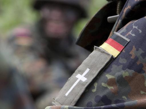 Schulterklappe mit Kreuz eines evangelischen Militärpfarrers unter einem Aufneher einer Deutschlandfahne auf der Schulter einer Camouflage Jacke