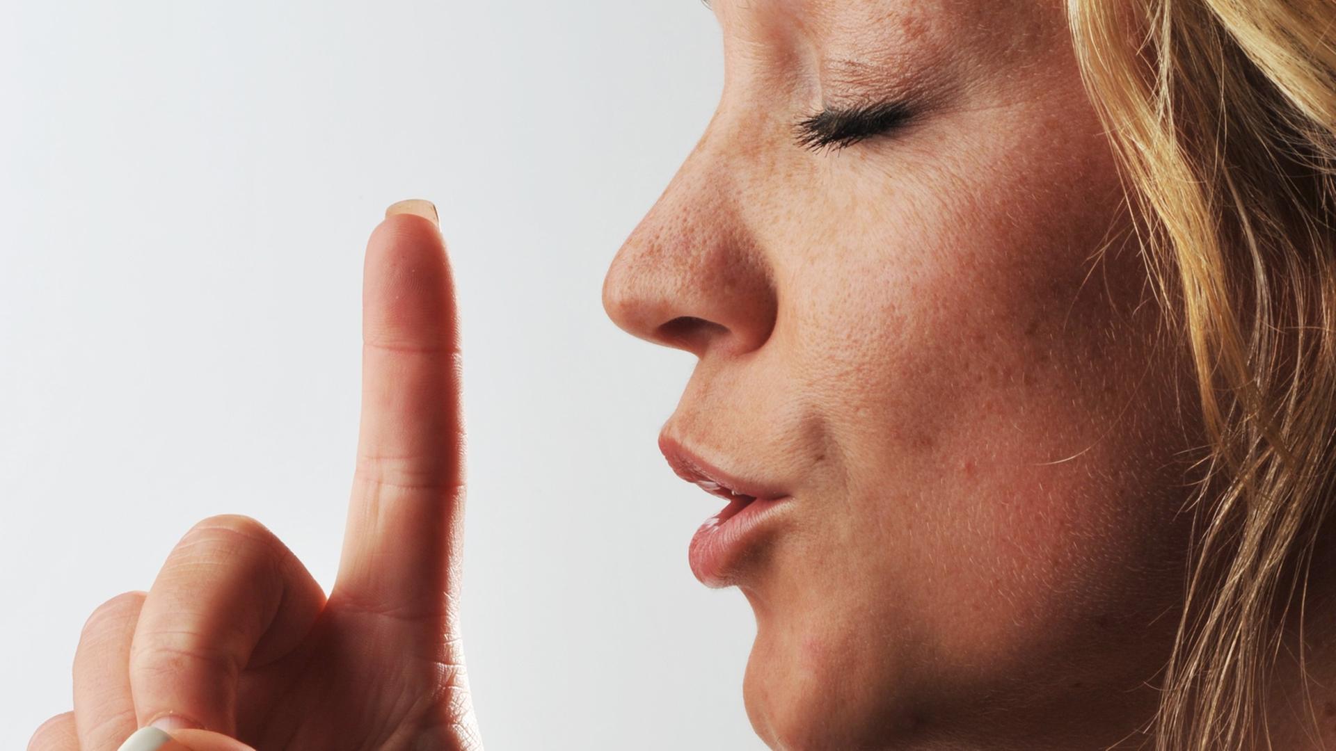 Eine Frau hält den Zeigefinger vor den Mund. Eine Frau hält den Zeigefinger vor den Mund.