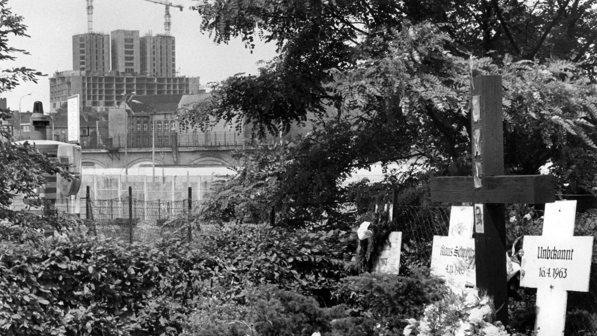 Blick von West-Berlin aus auf die Baustelle des chirurgischen Zentrums der Charité, im Bildvordergrund Gedenkkreuze für die Mauertoten.