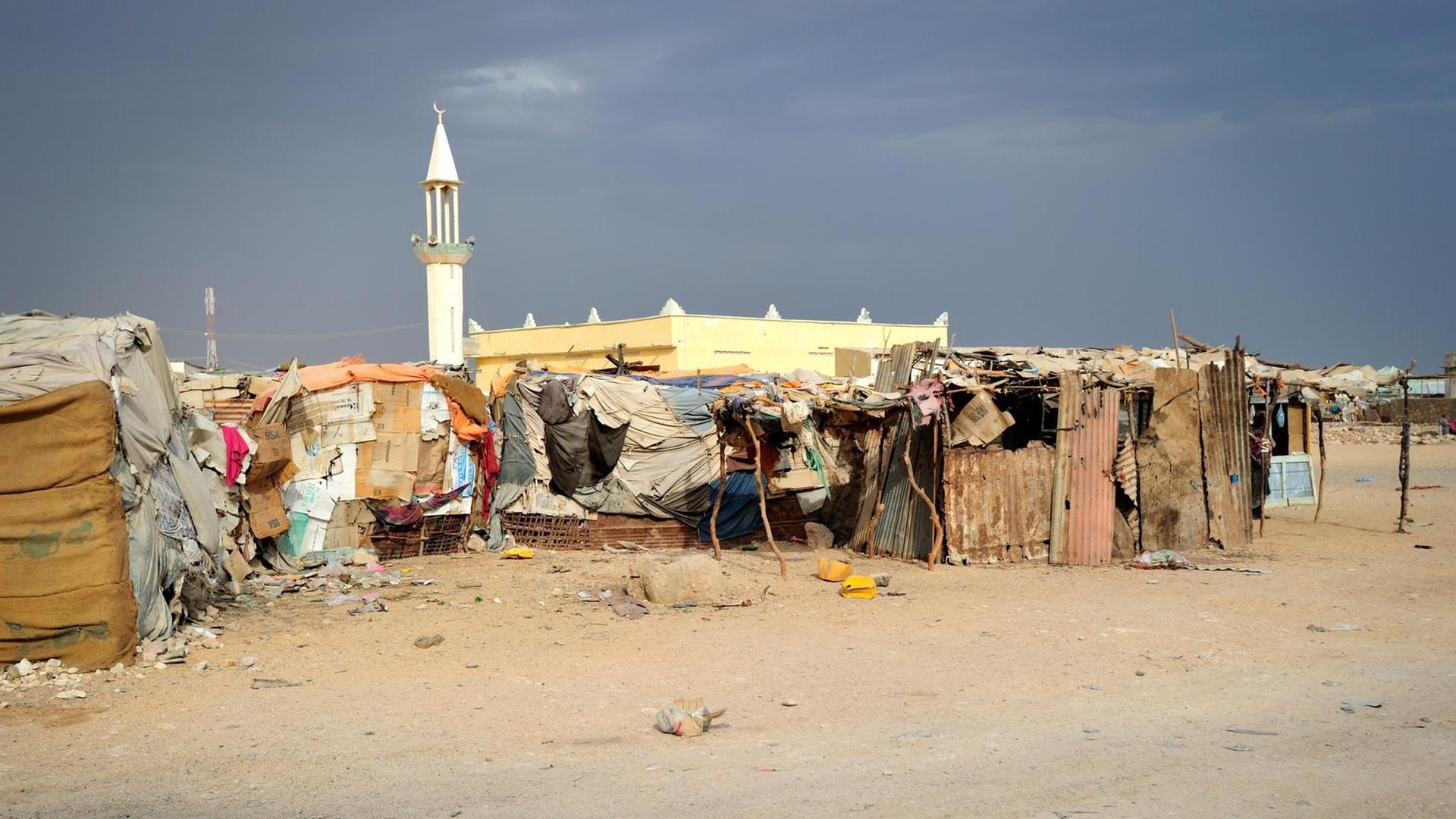 Eine Moschee mit Minarett im Hintergrund davor Hütten eines Flüchtlingslagers in Somalia.