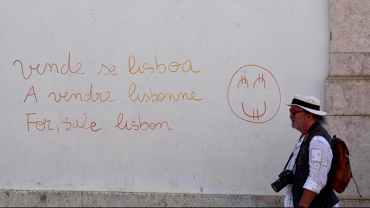 Touristen gehen in der Altstadt ovn Lissabon an einer Wand vorbei, auf der in mehreren Sprachen "Lissabon zu verkaufen" steht Touristen gehen in der Altstadt ovn Lissabon an einer Wand vorbei, auf der in mehreren Sprachen "Lissabon zu verkaufen" steht