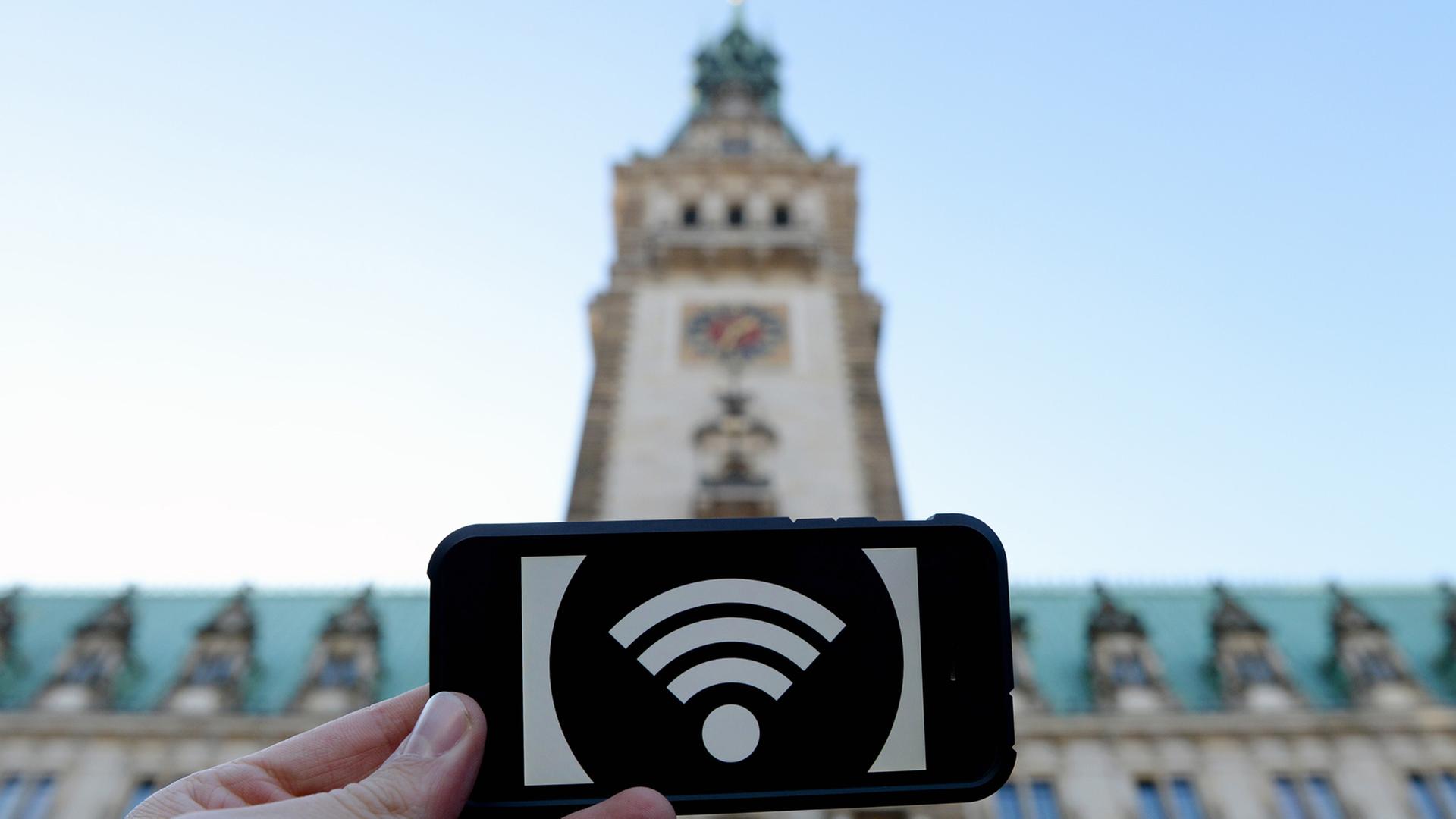 Eine Hand hält ein Schild mit einem WLAN-Symbol, im Hintergrund das Hamburger Rathaus. Eine Hand hält ein Schild mit einem WLAN-Symbol, im Hintergrund das Hamburger Rathaus.