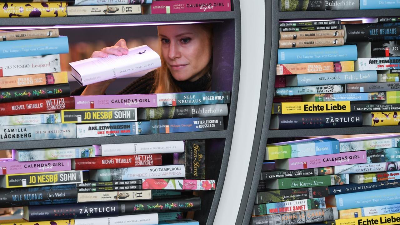 Die Frau stapelt Bücher in zwei Fenstern; ihr Kopf ist durch ein letztes verbliebenes Loch zwischen den Büchern zu sehen. Die Frau stapelt Bücher in zwei Fenstern; ihr Kopf ist durch ein letztes verbliebenes Loch zwischen den Büchern zu sehen.
