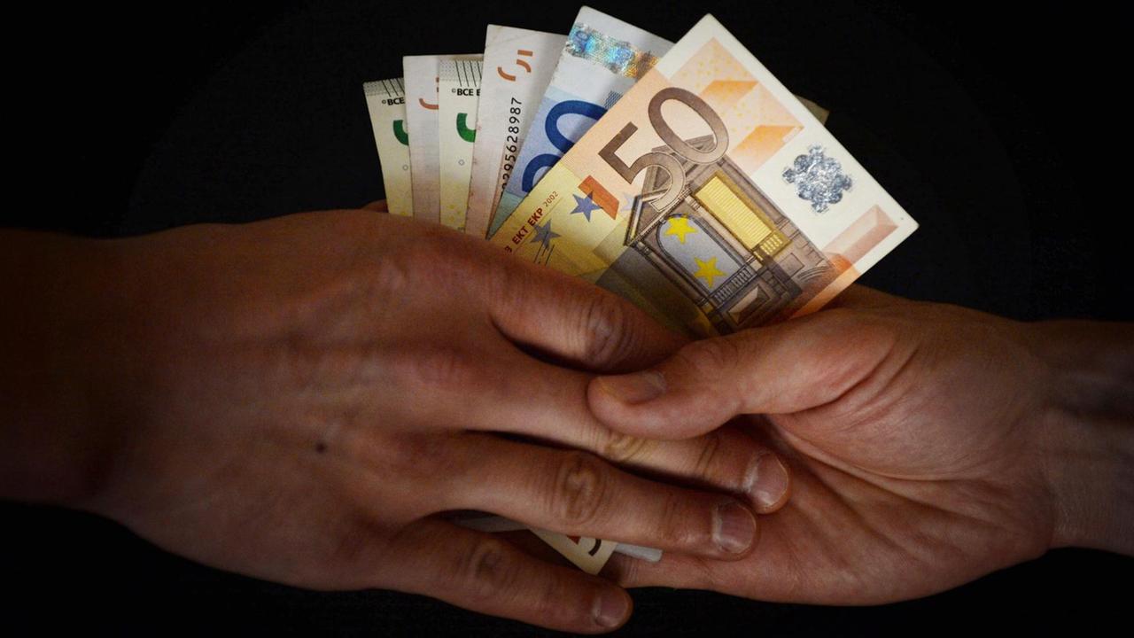 Zwei Hände. Die eine Hand gibt der andere mehrere Euroscheine. Zwei Hände. Die eine Hand gibt der andere mehrere Euroscheine.