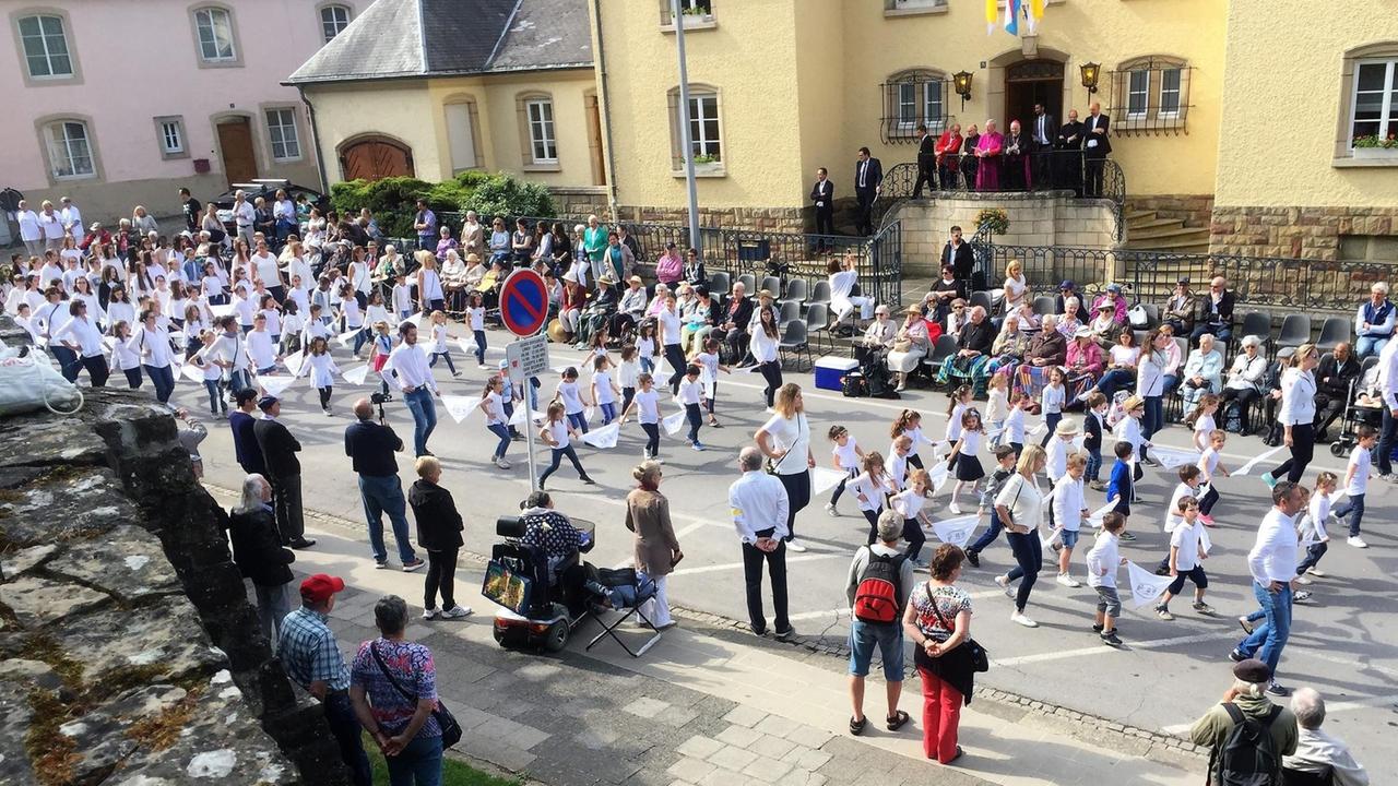 Weißgekleidete Kinder und Erwachsene bewegen sich durch die Strassen von Echternach. Traditionelle Echternacher Springprozession