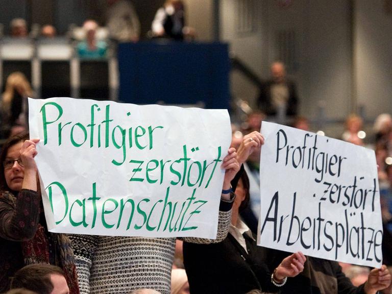 Demonstranten halten Transparente hoch, auf denen steht: Profitgier zerstört Datenschutz und Profitgier zerstört Arbeitsplätze.