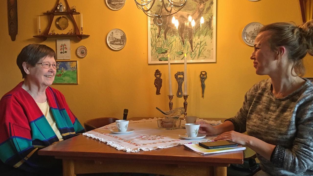 Birgit Breman sitzt mit einer Mitarbeiterin des kommunalen Pflegedienstes in ihrer Kopenhagener Wohnung vor den Kaffetassen an einem Tisch. Birgit Breman sitzt mit einer Mitarbeiterin des kommunalen Pflegedienstes in ihrer Kopenhagener Wohnung vor den Kaffetassen an einem Tisch.