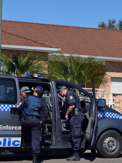Australische Polizisten steigen in einen Mannschaftswagen vor einem Wohnhaus.