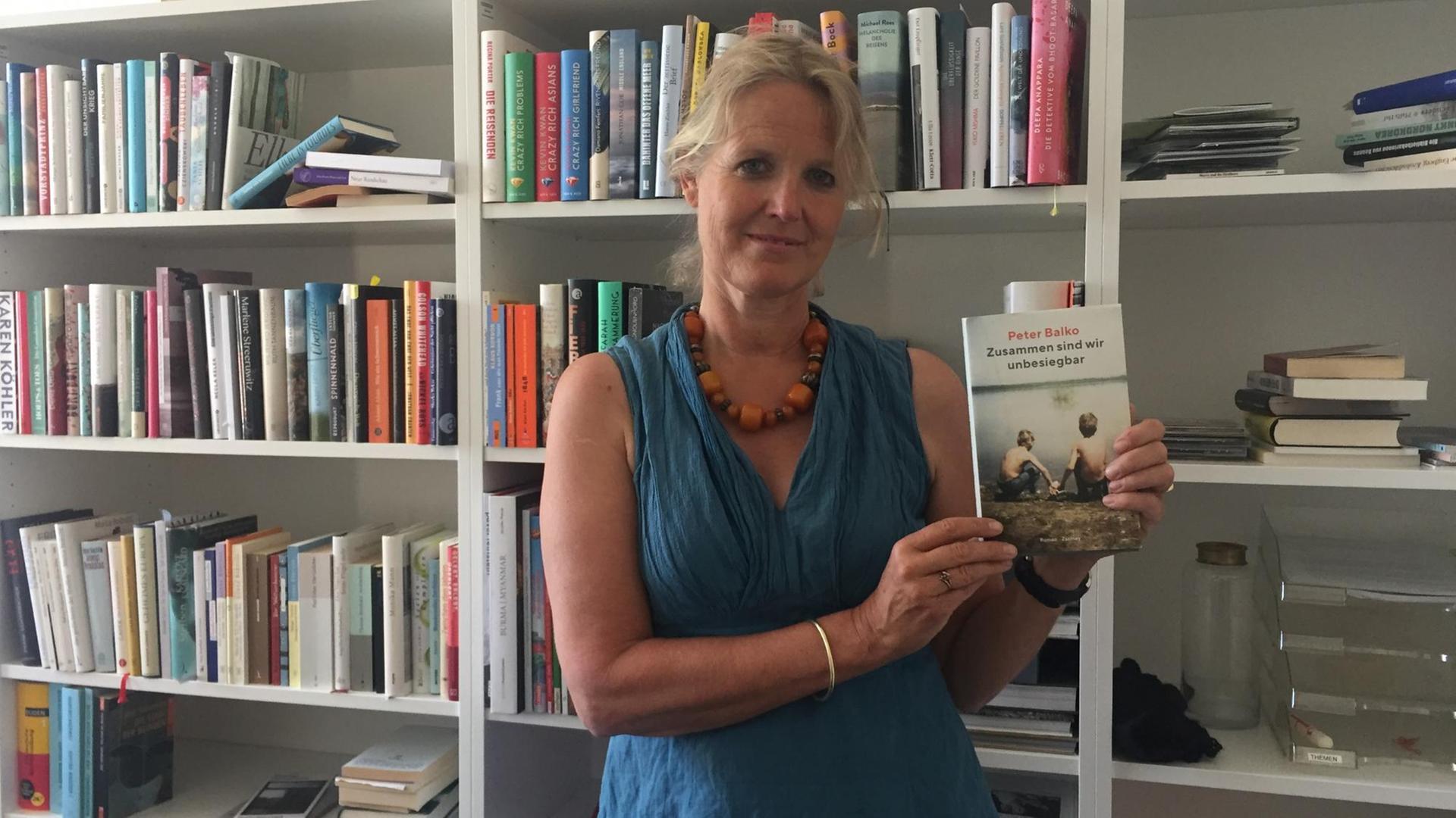 Literaturredakteurin Stephanie von Oppen vor einem Bücherregal mit dem Buch von Peter Balko in der Hand. Literaturredakteurin Stephanie von Oppen vor einem Bücherregal mit dem Buch von Peter Balko in der Hand.