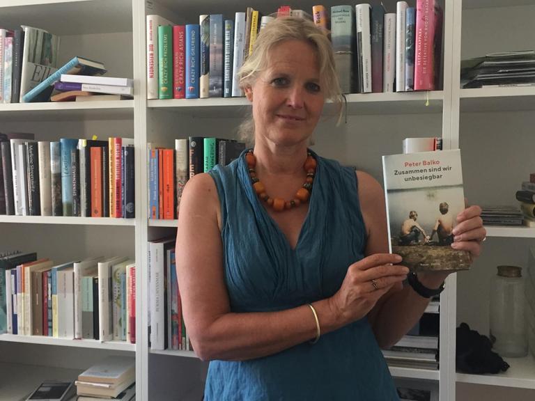 Literaturredakteurin Stephanie von Oppen vor einem Bücherregal mit dem Buch von Peter Balko in der Hand.