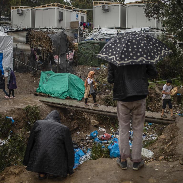 Ein Flüchtlingslager auf der griechischen Insel Lesbos im Regen: Menschen laufen durch Matsch, Müll liegt rum.