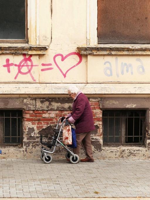 Eine Seniorin mit einem Rollator geht an Graffiti an einem leerstehenden Altbau in der Innenstadt von Dessau vorbei.