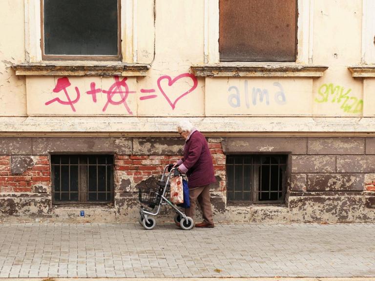 Eine Seniorin mit einem Rollator geht an Graffiti an einem leerstehenden Altbau in der Innenstadt von Dessau vorbei.