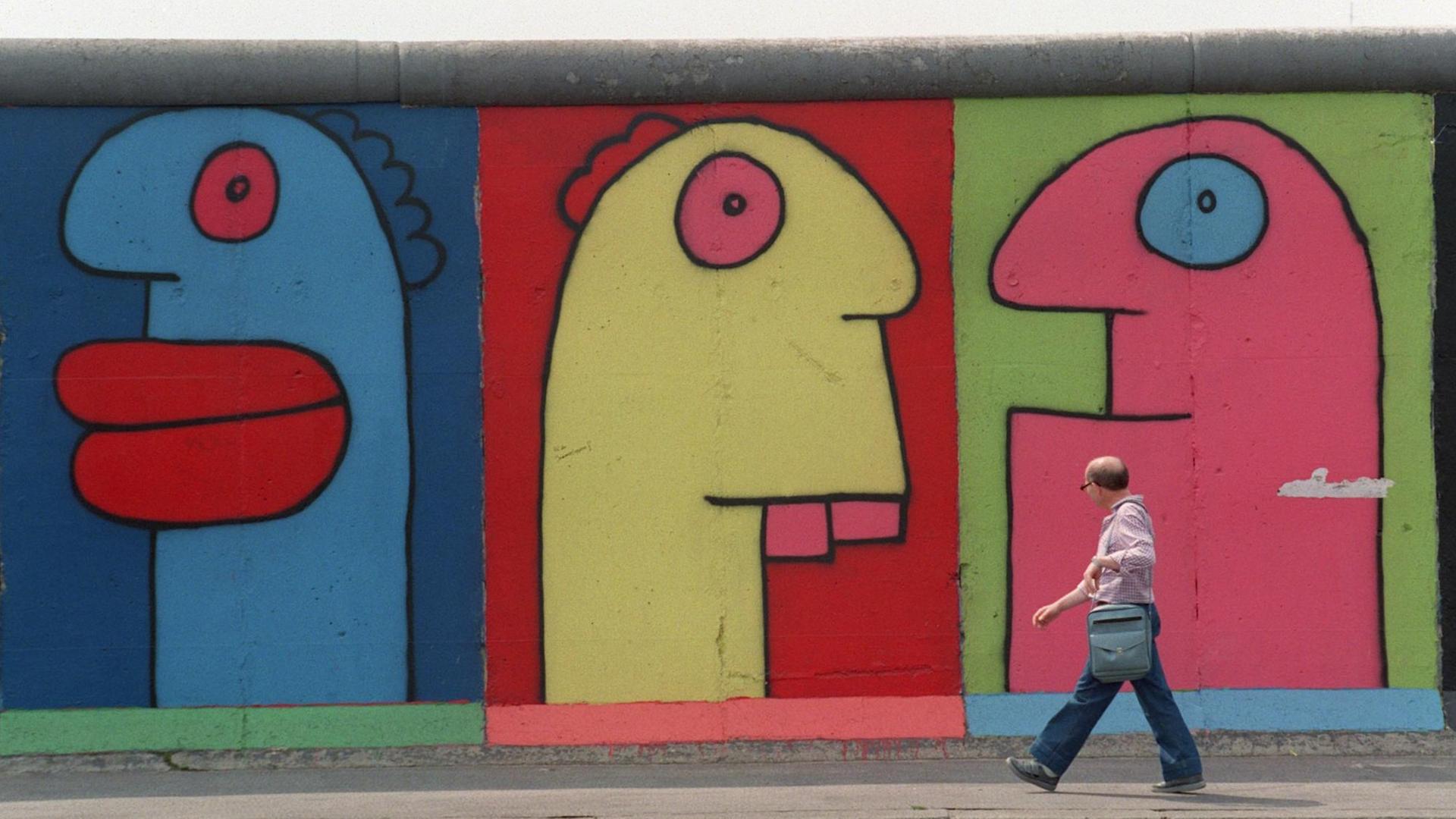 Menschen gehen im Berliner Bezirk Friedrichshain an der East Side Gallery (ehemalige Berliner Mauer) vorbei, auf denen Figuren des Künstlers Thierry Noir zu sehen sind. Menschen gehen im Berliner Bezirk Friedrichshain an der East Side Gallery (ehemalige Berliner Mauer) vorbei, auf denen Figuren des Künstlers Thierry Noir zu sehen sind.