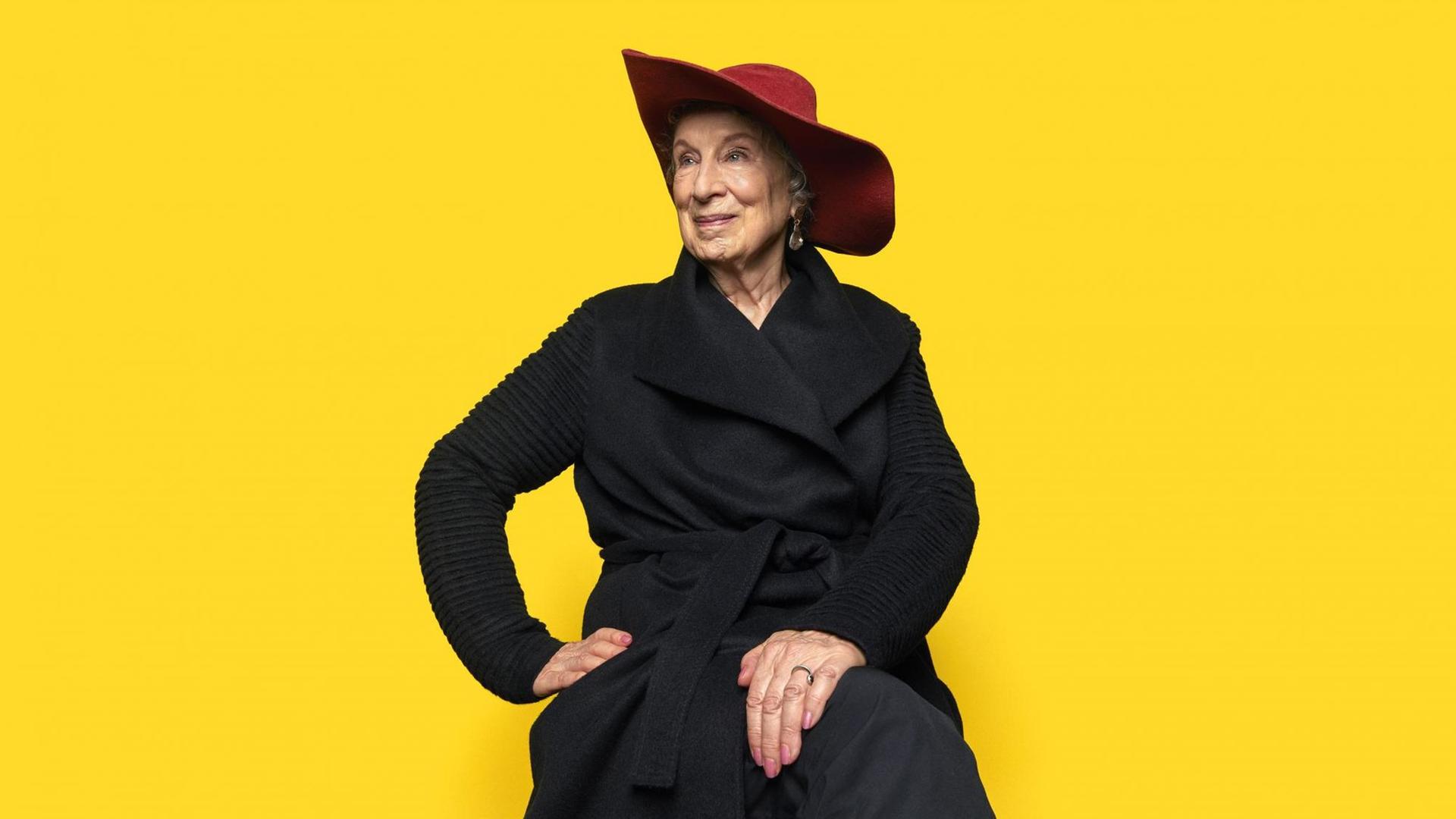 Ein Porträtfoto zeigt Margaret Atwood mit rotem Hut vor einem gelben Hintergrund. Geboren 1939 in Ottawa, gehört zu den bedeutendsten Erzählerinnen unserer Zeit. Ein Porträtfoto zeigt Margaret Atwood mit rotem Hut vor einem gelben Hintergrund. Geboren 1939 in Ottawa, gehört zu den bedeutendsten Erzählerinnen unserer Zeit.