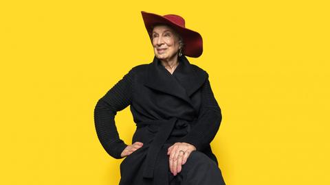 Ein Porträtfoto zeigt Margaret Atwood mit rotem Hut vor einem gelben Hintergrund. Geboren 1939 in Ottawa, gehört zu den bedeutendsten Erzählerinnen unserer Zeit.