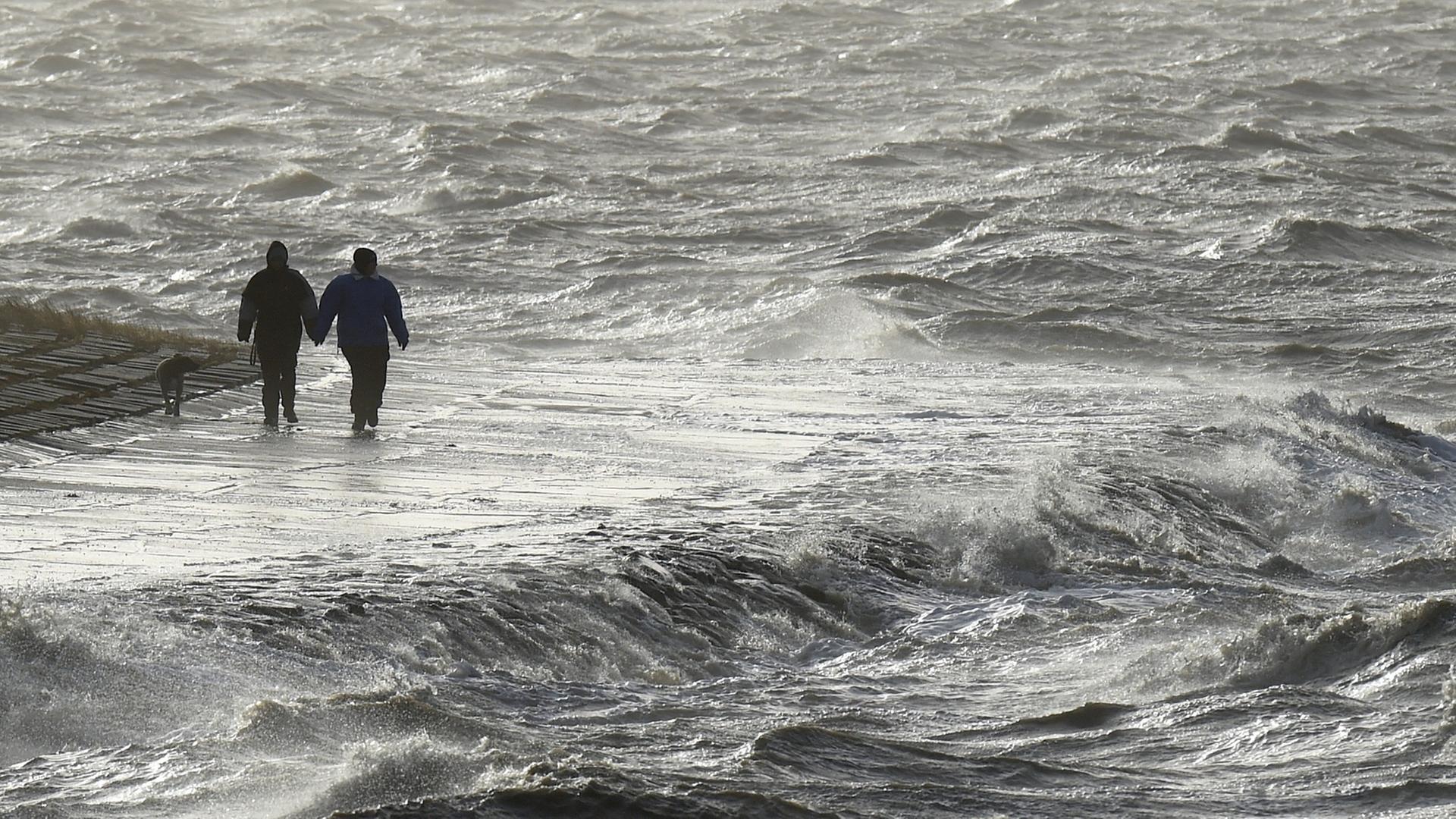 Passanten trotzen am 09.01.2015 in Dagebüll (Schleswig-Holstein) am Nordseedeich dem Sturm. Gleich zwei Orkanausläufer werden an diesem Wochenende den Norden streifen. Passanten trotzen am 09.01.2015 in Dagebüll (Schleswig-Holstein) am Nordseedeich dem Sturm. Gleich zwei Orkanausläufer werden an diesem Wochenende den Norden streifen.