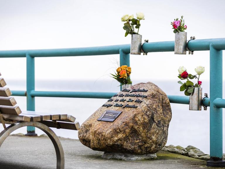 Das Bild zeigt einen Gedenkstein der Reederei Huntemann an der Mohle Hooksiel, mit dem an die Toten einer Seebestattung auf der Nordsee gedacht wird. Es sind Blumen angebracht. Dahinter erstreckt sich die See.