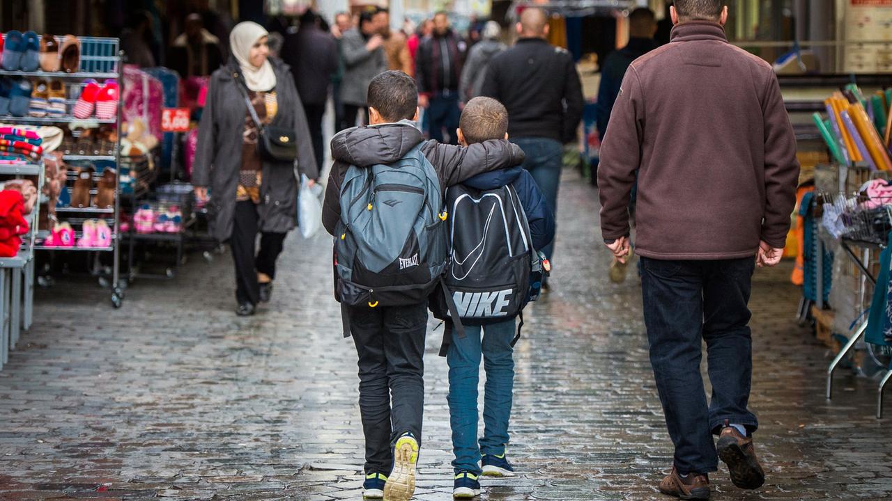 Zwei Jungen mit Rucksack laufen Arm in Arm durch eine Einkaufsstraße im Brüsseler Stadtteil Molenbeek, aufgenommen 2015 Zwei Jungen mit Rucksack laufen Arm in Arm durch eine Einkaufsstraße im Brüsseler Stadtteil Molenbeek, aufgenommen 2015