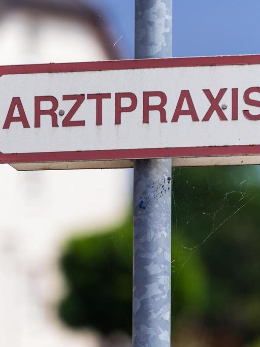 Ein Schild „Arztpraxis“ steht an der Straße.