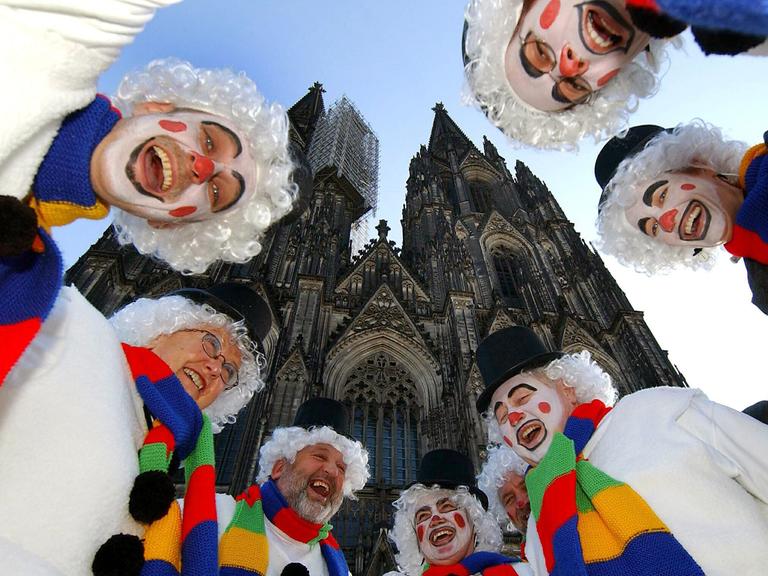 Als Schneemänner verkleidete Jecken lachen beim Karneval vor dem Dom in Köln.