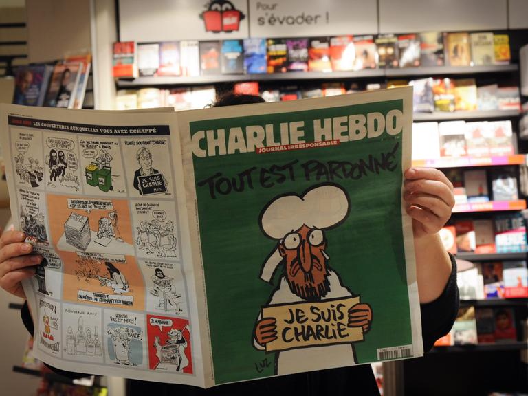 Eine Person liest in einem Pariser Kiosk die aktuelle Ausgabe der Satire-Zeitschrift "Charlie Hebdo" (14.01.2015)