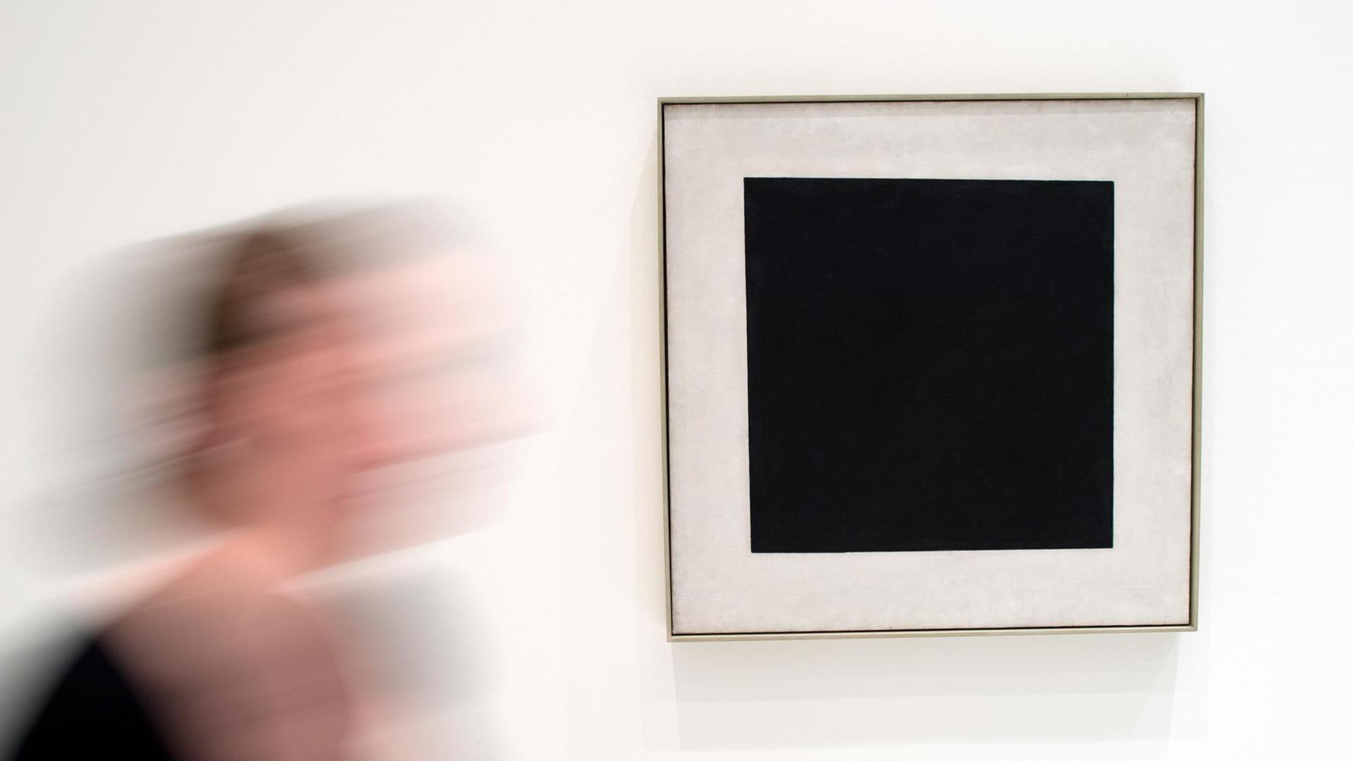 Eine Museumsmitarbeiterin geht am 01.04.2014 in Düsseldorf (Nordrhein-Westfalen) am Bild "Schwarzes Quadrat" von Kasimir Malewitsch aus dem Jahr 1929 vorbei. Die Ausstellung "Kandinsky, Malewitsch, Mondrian _ Der weiße Abgrund Unendlichkeit" zeigt im Rahmen der Quadrinale 2014 im K20 vom 05.04. - 06.07.2014 Werke der drei Künstler, die sich mit der Farbe Weiß auseinander setzen. Foto: Federico Gambarini/dpa | Verwendung weltweit Eine Museumsmitarbeiterin geht am 01.04.2014 in Düsseldorf (Nordrhein-Westfalen) am Bild "Schwarzes Quadrat" von Kasimir Malewitsch aus dem Jahr 1929 vorbei. Die Ausstellung "Kandinsky, Malewitsch, Mondrian _ Der weiße Abgrund Unendlichkeit" zeigt im Rahmen der Quadrinale 2014 im K20 vom 05.04. - 06.07.2014 Werke der drei Künstler, die sich mit der Farbe Weiß auseinander setzen. Foto: Federico Gambarini/dpa | Verwendung weltweit