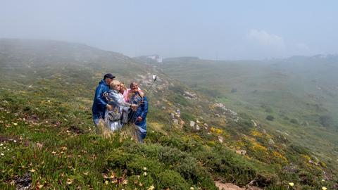 Eine Reisegruppe fotografiert sich in Portugal auf einer hügeligen grünen Wiese.