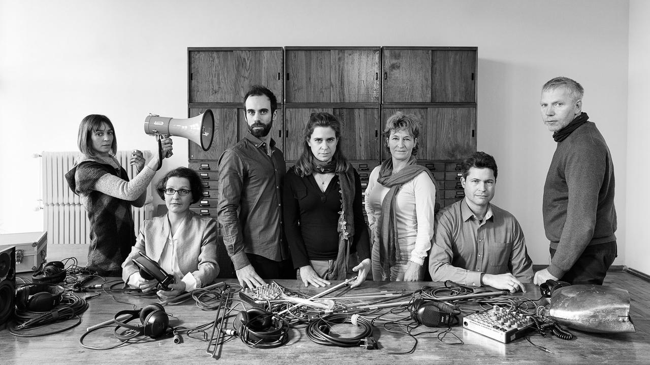 Das Schwarzweiß-Foto zeigt eine Gruppe von Musikern mit Instrumenten und unkonventionellen Geräten