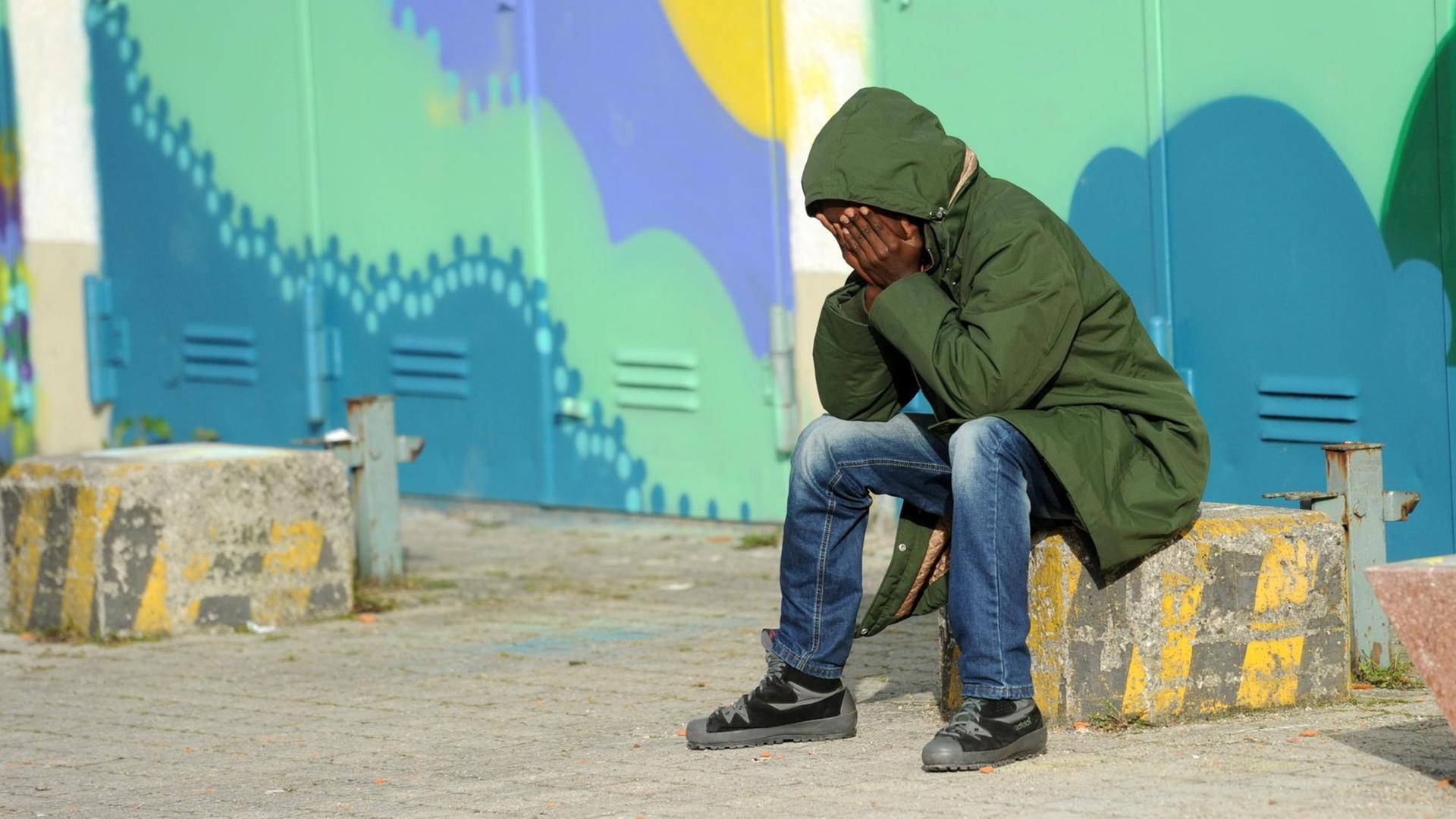 Ein Flüchtling aus Eritrea sitzt am 31.10.2014 in München (Bayern) in der Erstaufnahmeeinrichtung für Asylbewerber auf dem Gelände der Bayernkaserne vor bunt bemalten Hallentoren. Ein Flüchtling aus Eritrea sitzt am 31.10.2014 in München (Bayern) in der Erstaufnahmeeinrichtung für Asylbewerber auf dem Gelände der Bayernkaserne vor bunt bemalten Hallentoren.