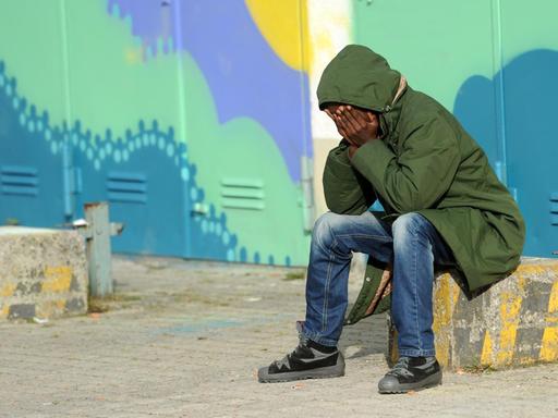 Ein Flüchtling aus Eritrea sitzt am 31.10.2014 in München (Bayern) in der Erstaufnahmeeinrichtung für Asylbewerber auf dem Gelände der Bayernkaserne vor bunt bemalten Hallentoren.