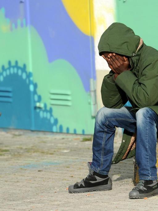Ein Flüchtling aus Eritrea sitzt am 31.10.2014 in München (Bayern) in der Erstaufnahmeeinrichtung für Asylbewerber auf dem Gelände der Bayernkaserne vor bunt bemalten Hallentoren.