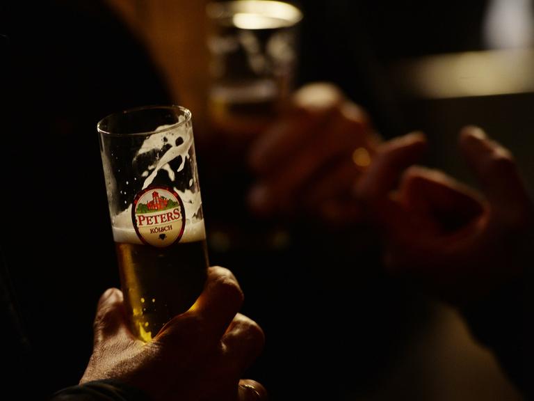 Ein Mann hält ein Kölsch-Glas in der Hand.