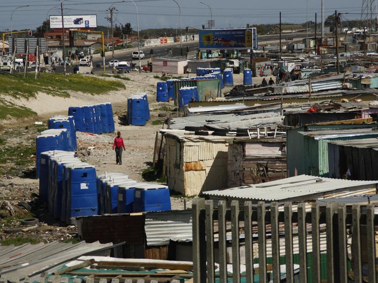 Das Bild zeigt eine südafrikanische Armensiedlung, an deren Rand eine Reihe von Toilettenhäuschen stehen