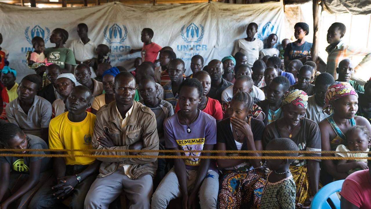 Flüchtlinge aus dem Sudan in einem UNHCR-Registrierungszentrum in Uganda im Mai 2018. Menschen warten in einem Zelt.
