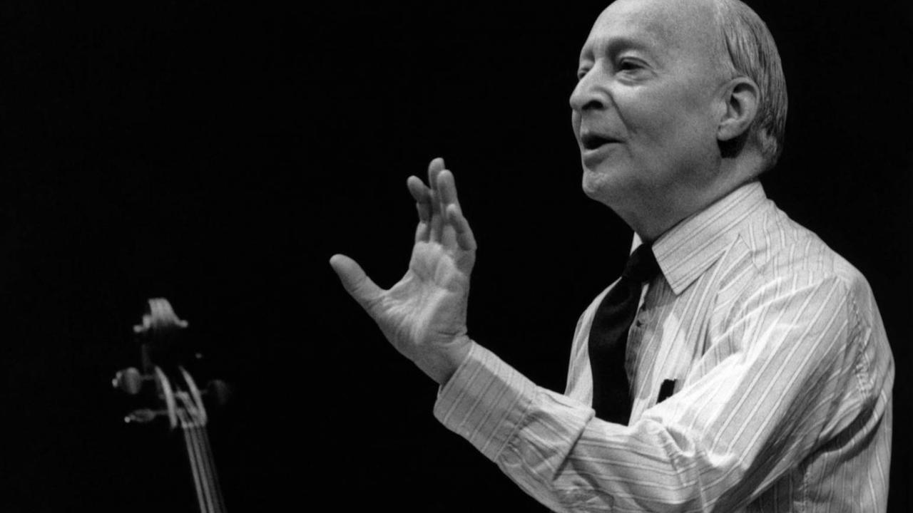 Ein älterer Mann steht dirigierend vor einem Orchester. Ein älterer Mann steht dirigierend vor einem Orchester.