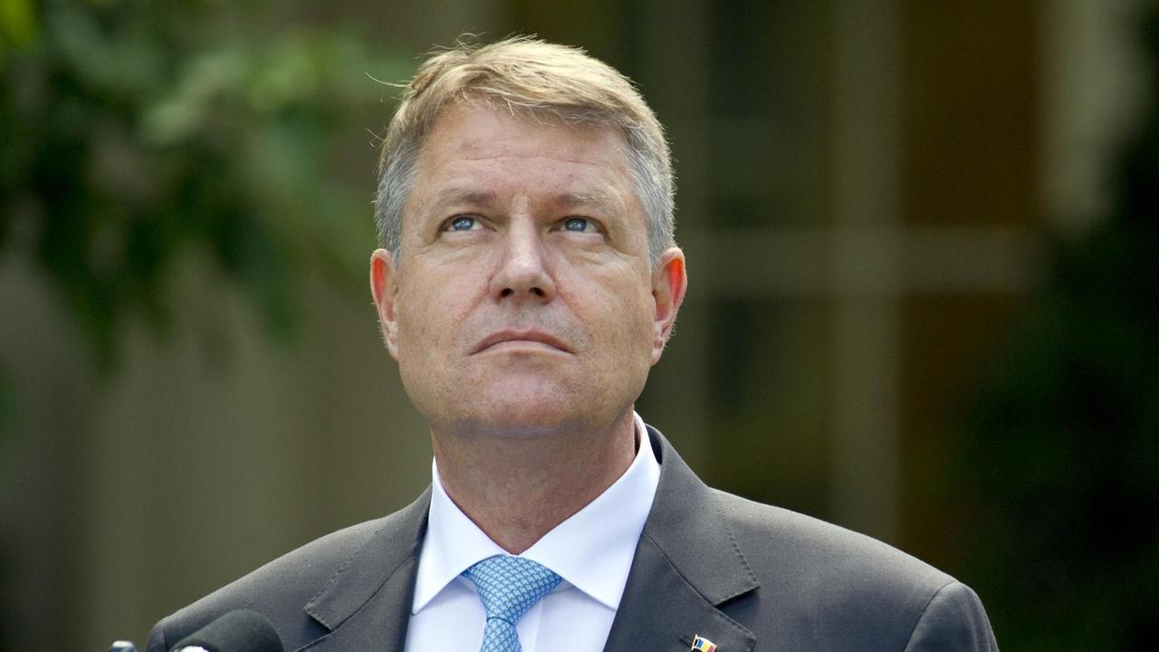 Iohannis steht vor einem Mikrofon und schaut mit ernstem Blick nach oben. Iohannis steht vor einem Mikrofon und schaut mit ernstem Blick nach oben.