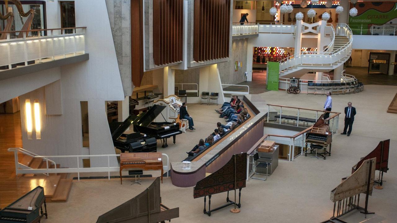 Blick in einen hohen modernen Raum mit Treppen zu Galeriegängen, in dem zahlreiche Tasteninstrumente aufgestellt sind. Blick in einen hohen modernen Raum mit Treppen zu Galeriegängen, in dem zahlreiche Tasteninstrumente aufgestellt sind.